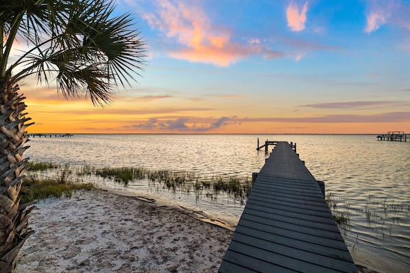 A wooden pier extending into calm waters, surrounded by sand and sparse vegetation.
