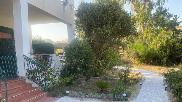 Un vialetto fiorito conduce all'ingresso di un edificio, con gradini e ringhiera.