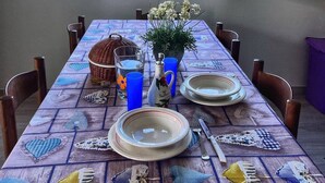 Tavola imbandita con piatti, posate e un vaso di fiori, vista su un paesaggio rurale attraverso una finestra.