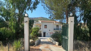 Un ingresso recintato a un edificio con tetto in tegole, immerso nel verde sotto un cielo sereno.