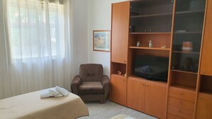 Una stanza con due lettini da massaggio, un armadio in legno con vetrine, una sedia e un quadro appeso al muro.