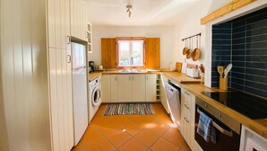 Eine kompakte Küche mit Waschmaschine, Kühlschrank, einer Holzauskładung und einer schwarzen, gefliesten Spritzschutzwand.