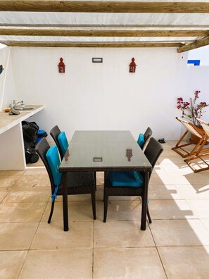 Uma área de refeições com mesa e cadeiras, um pequeno espaço de cozinha com pia e uma planta decorativa.