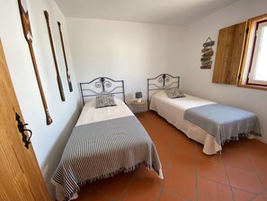 Quarto com duas camas, uma pequena mesa de cabeceira com abajur e uma parede com ripas de madeira e uma placa.