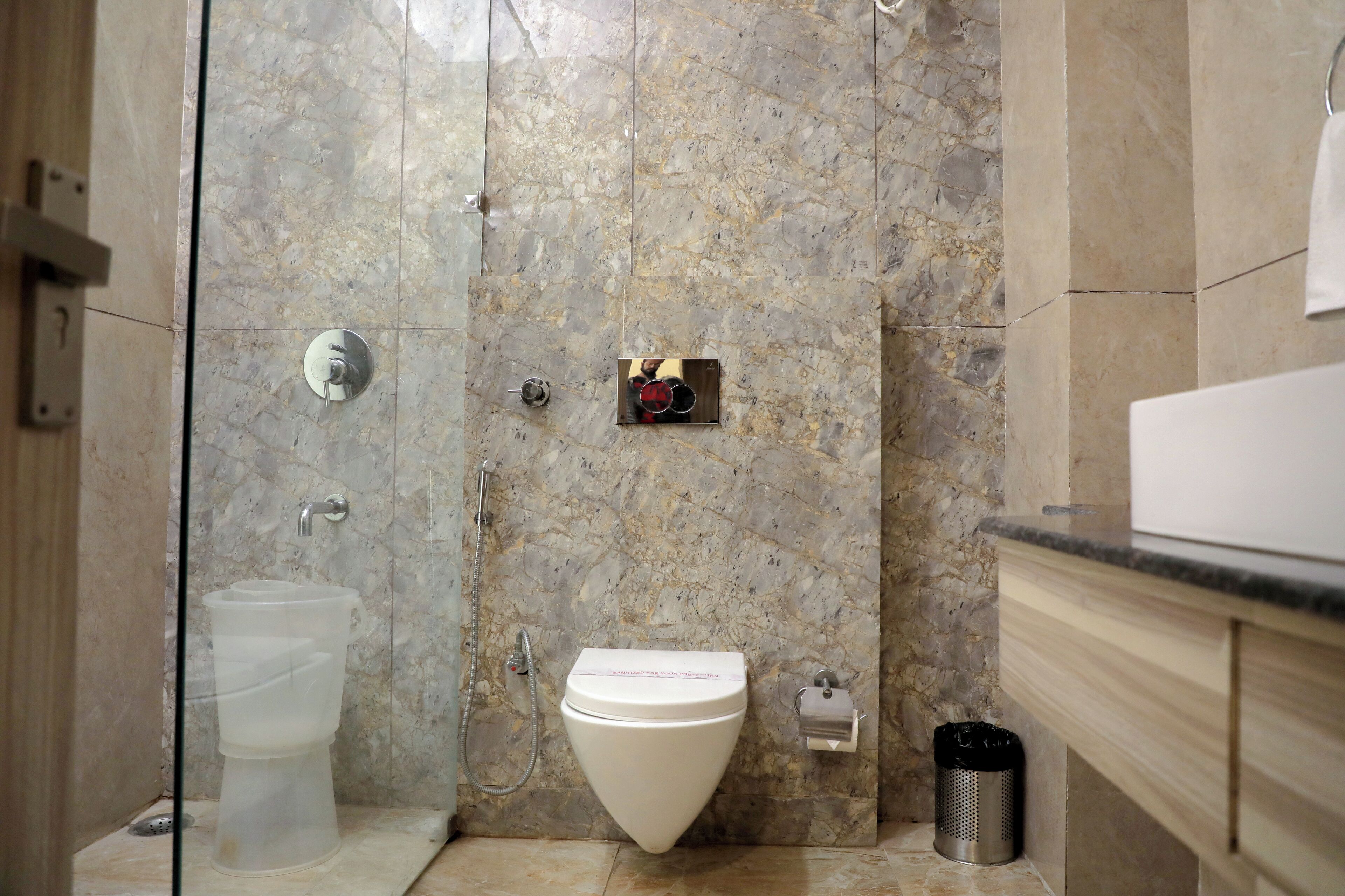 Een badkamer met een marmeren wand, een toilet, een bidet, een prullenbak en een handdoekhouder.