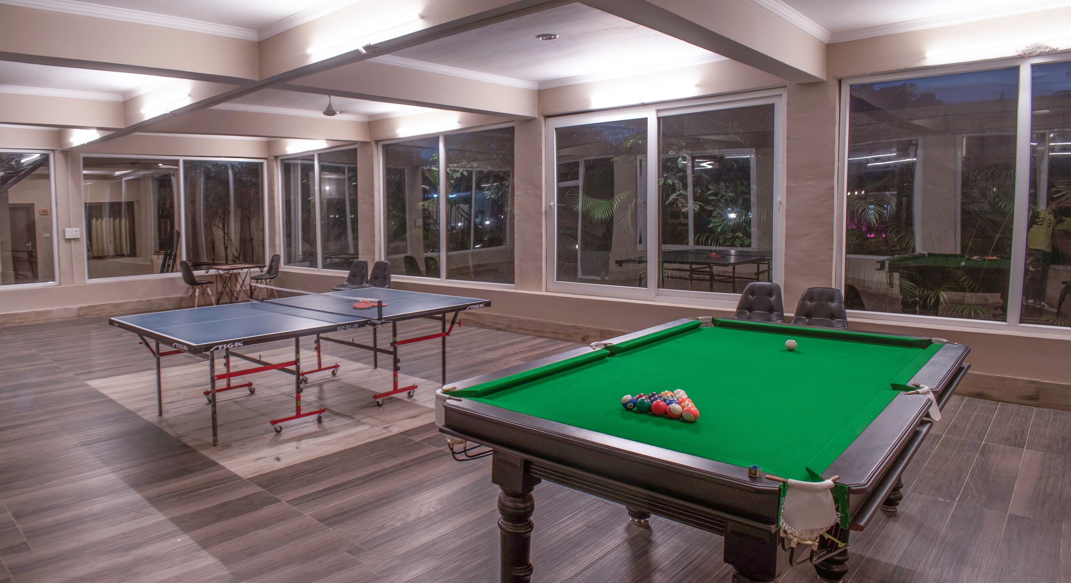 Une salle de billard équipée de deux tables de ping-pong et d’une table de billard, avec de grandes fenêtres et un plancher en bois.