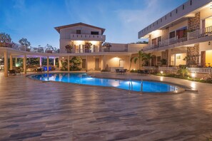 A pool area with a pool, lounge chairs, and a building with balconies. - Vow Resorts And Spa (Kaladhungi)