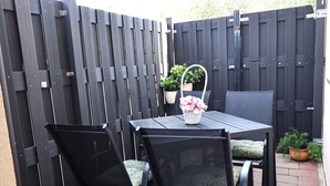 En terrasse med et bord og stole, et sort hegn og krukker med planter.