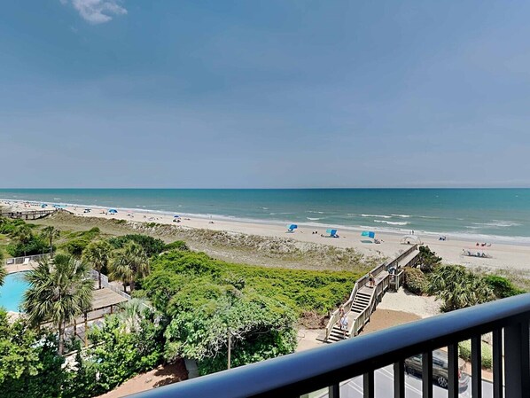 Une vue sur la plage, avec une promenade en bois menant au rivage, une piscine et une végétation luxuriante.