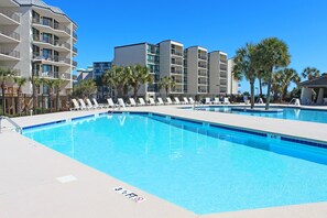 Une piscine entourée de bâtiments à plusieurs étages, avec des chaises longues et des palmiers.