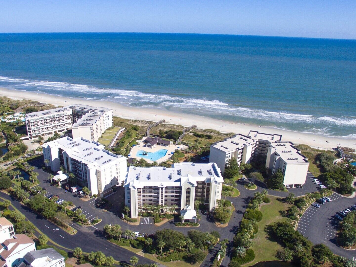 An aerial view of a coastal hotel complex with multiple buildings, a swimming pool, and a beach in the background.