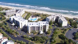 Vista aerea di un complesso alberghiero costiero con diversi edifici, una piscina e una spiaggia sullo sfondo.