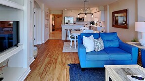 Un soggiorno moderno con un divano blu, pavimento in legno e una cucina sullo sfondo.