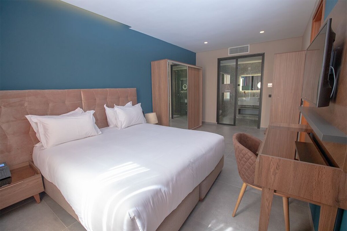 A modern hotel room with a large bed, a desk, and a wardrobe.