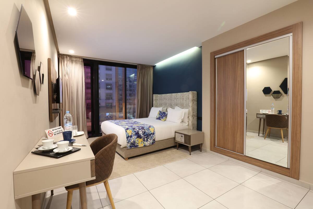 Una habitación de hotel moderna con una cama grande, un escritorio con silla, un armario y vistas a la ciudad de noche.