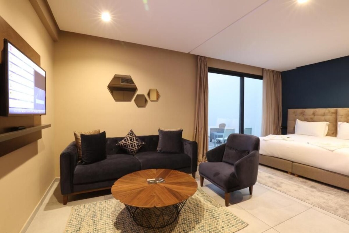 A modern hotel room with a sofa, armchair, round coffee table, and a bed.