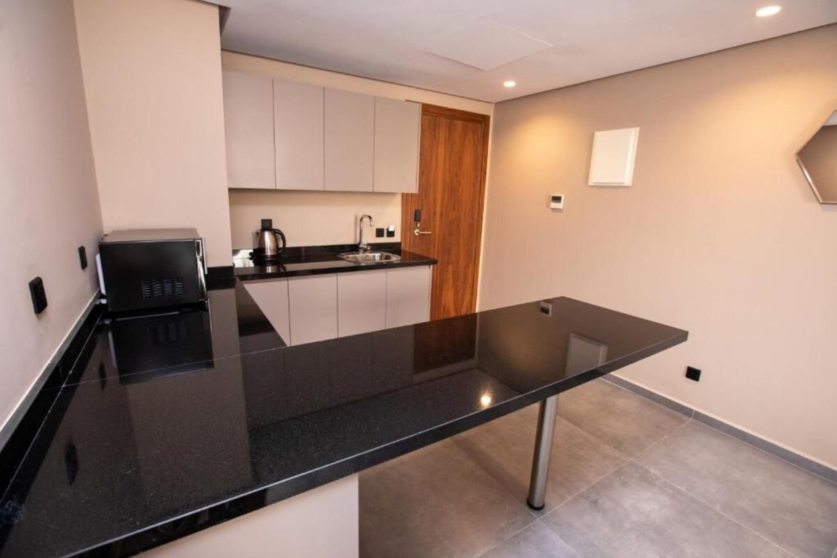 A modern kitchen with a black countertop, stainless steel appliances, and a wooden door.