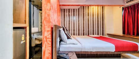 A compact hotel room with a bed, a small desk, a mirror, and a wardrobe.