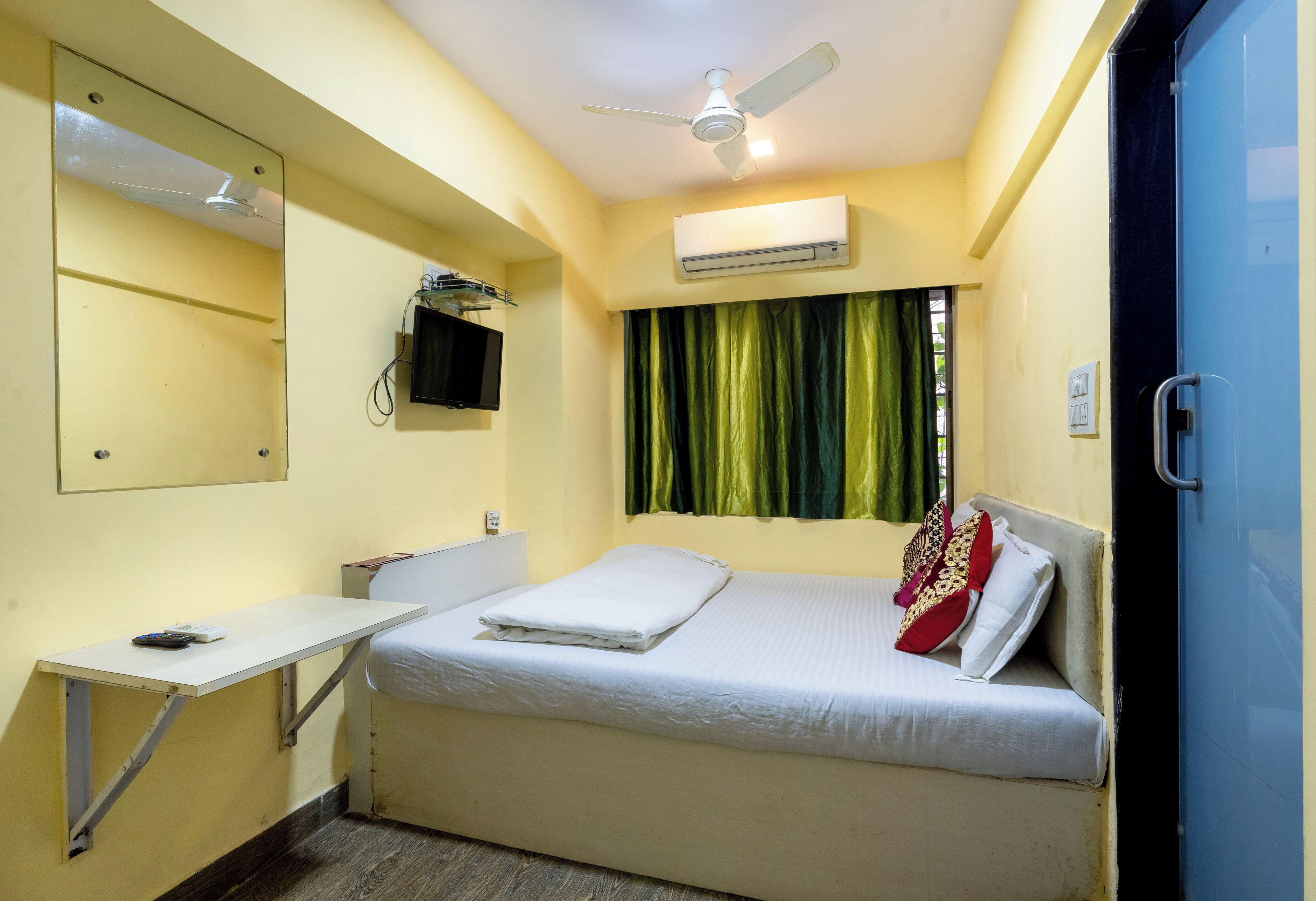 Ein Zimmer mit Bett, Schreibtisch, Deckenventilator, Klimaanlage und einem Vorhangfenster.