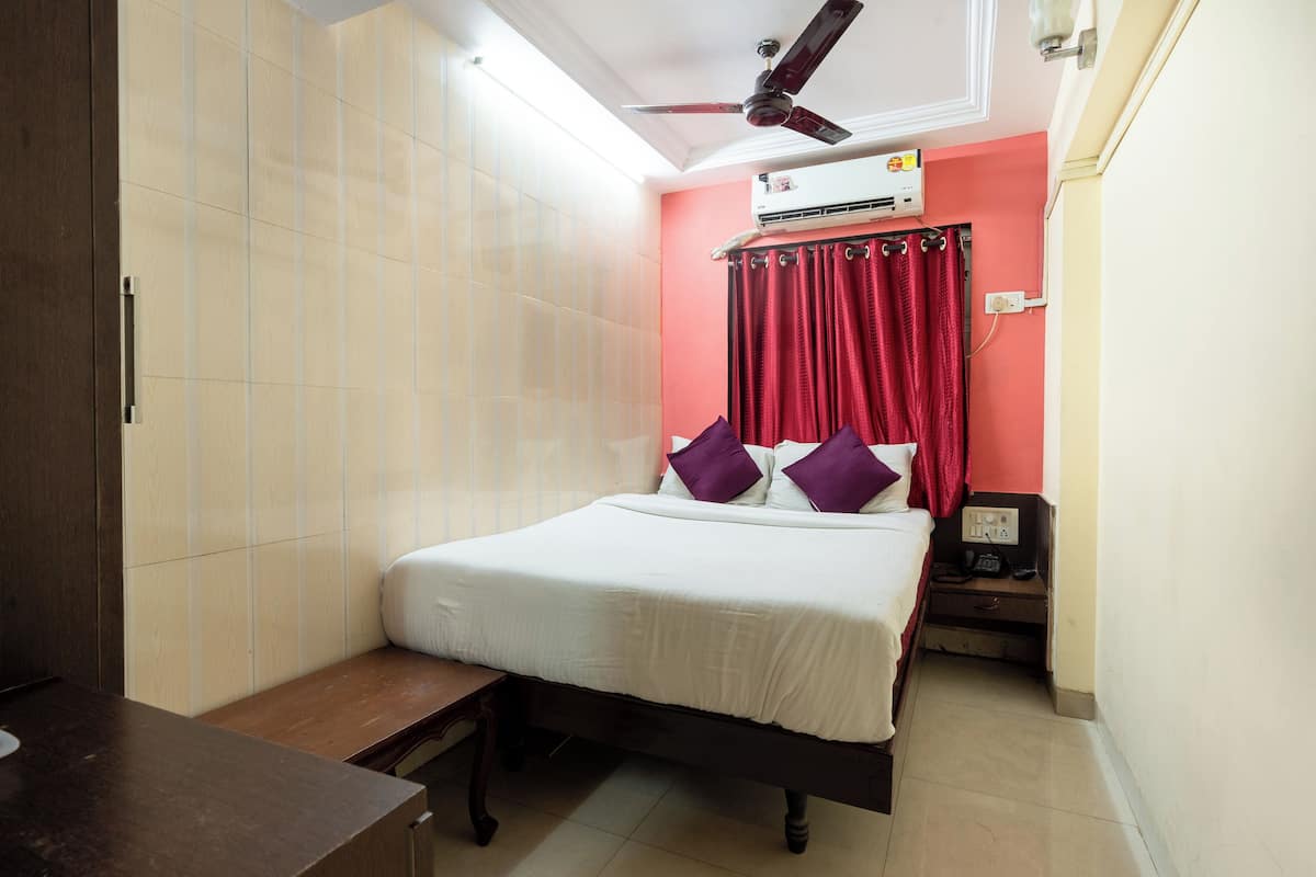 A bedroom with a bed, a nightstand, a desk, a ceiling fan, and an air conditioning unit.