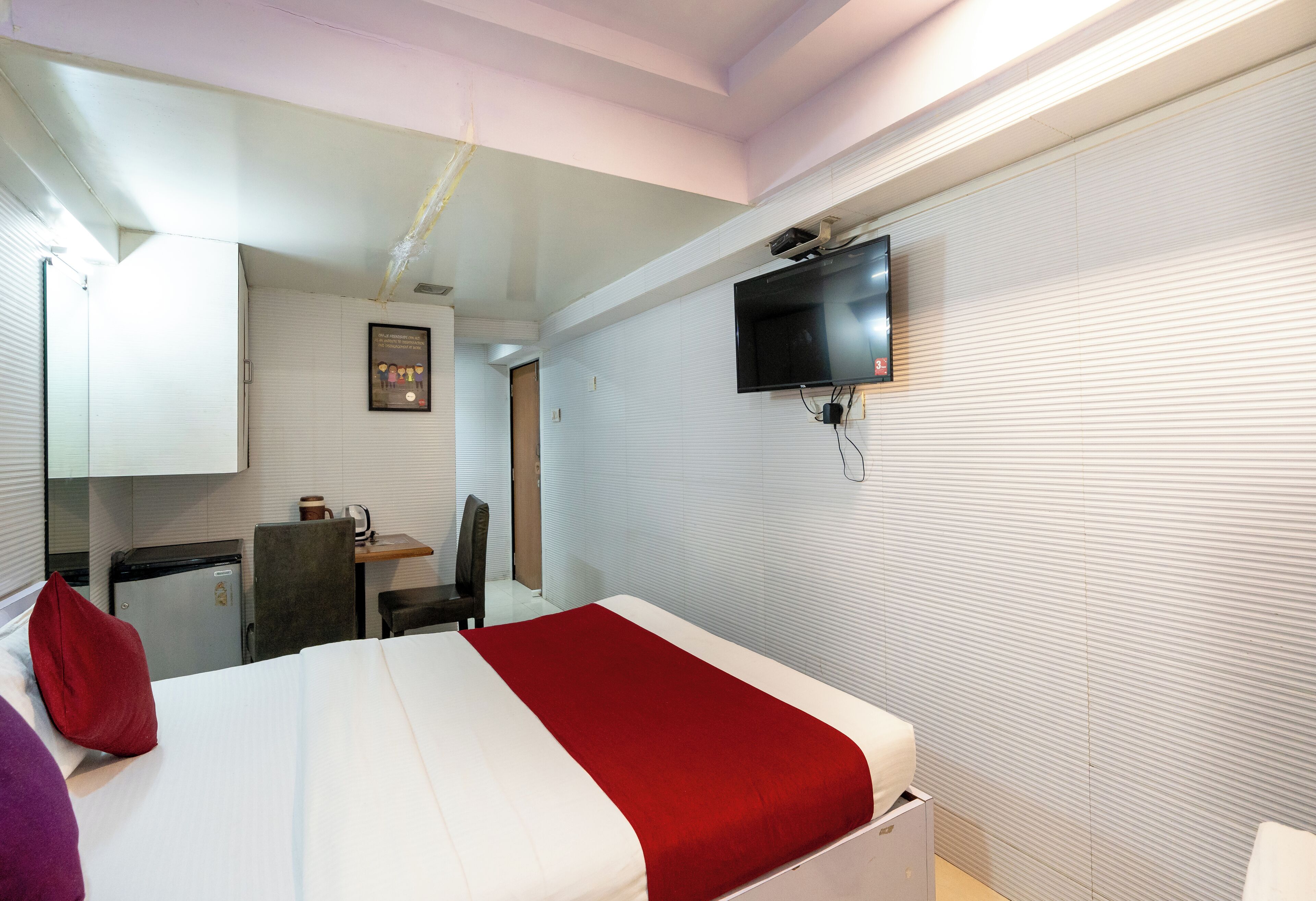 A hotel room with a bed, a desk, a chair, a television mounted on the wall, and a small refrigerator.