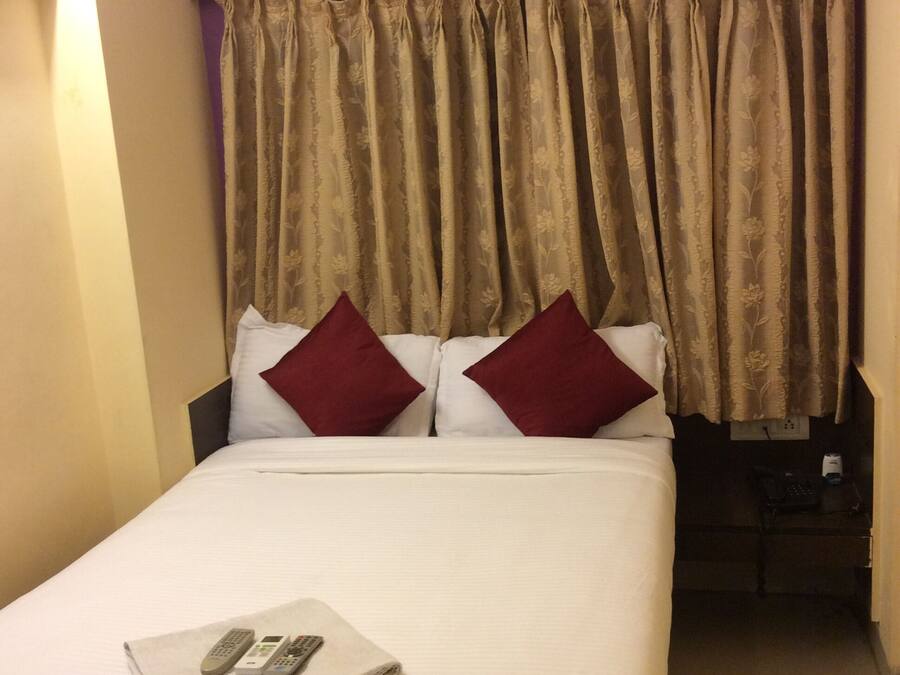 A hotel room with a bed, two red pillows, a white blanket, and a remote control on the bed.