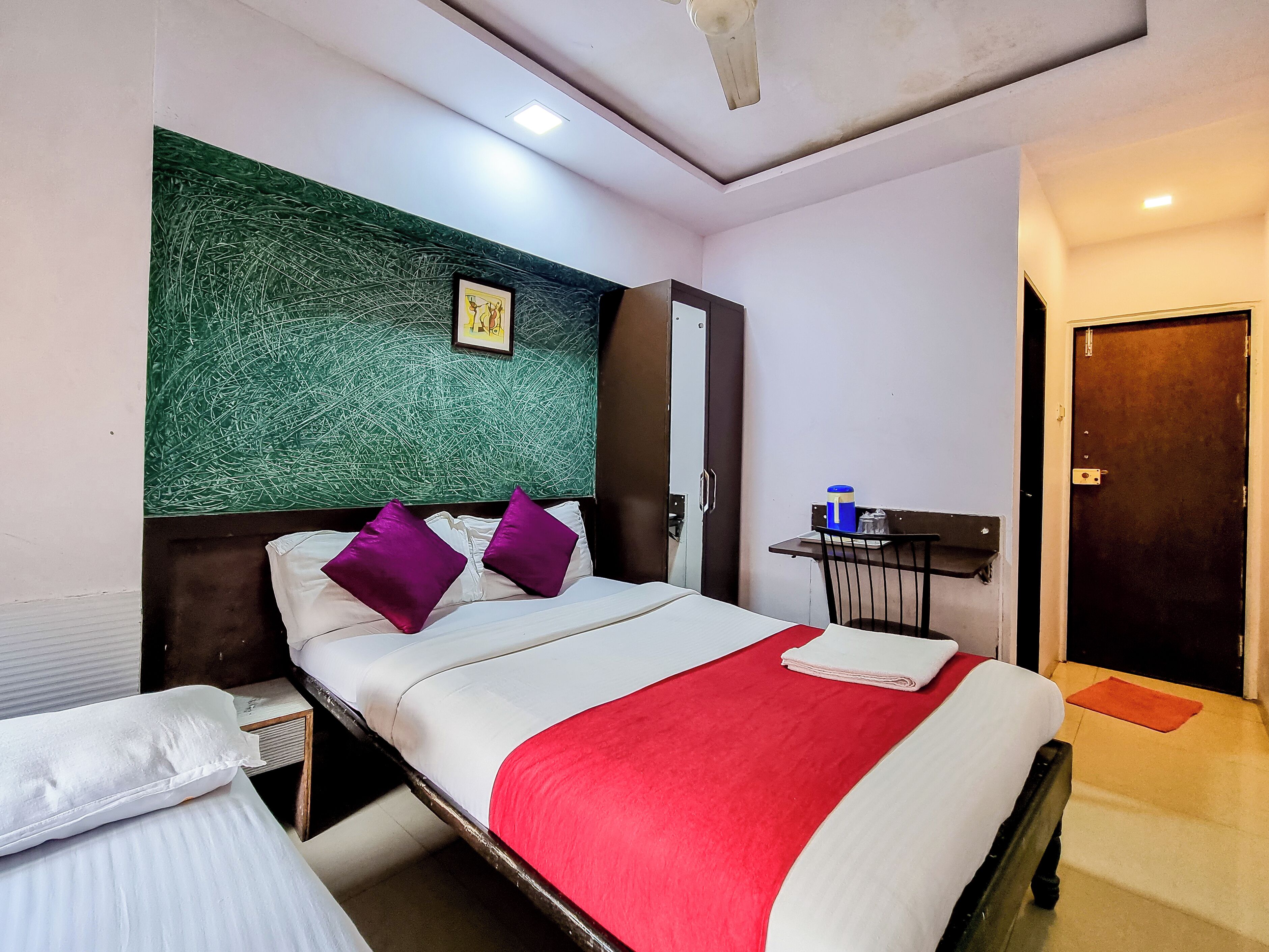 A hotel room with a bed, a nightstand, a desk, and a green textured wall.