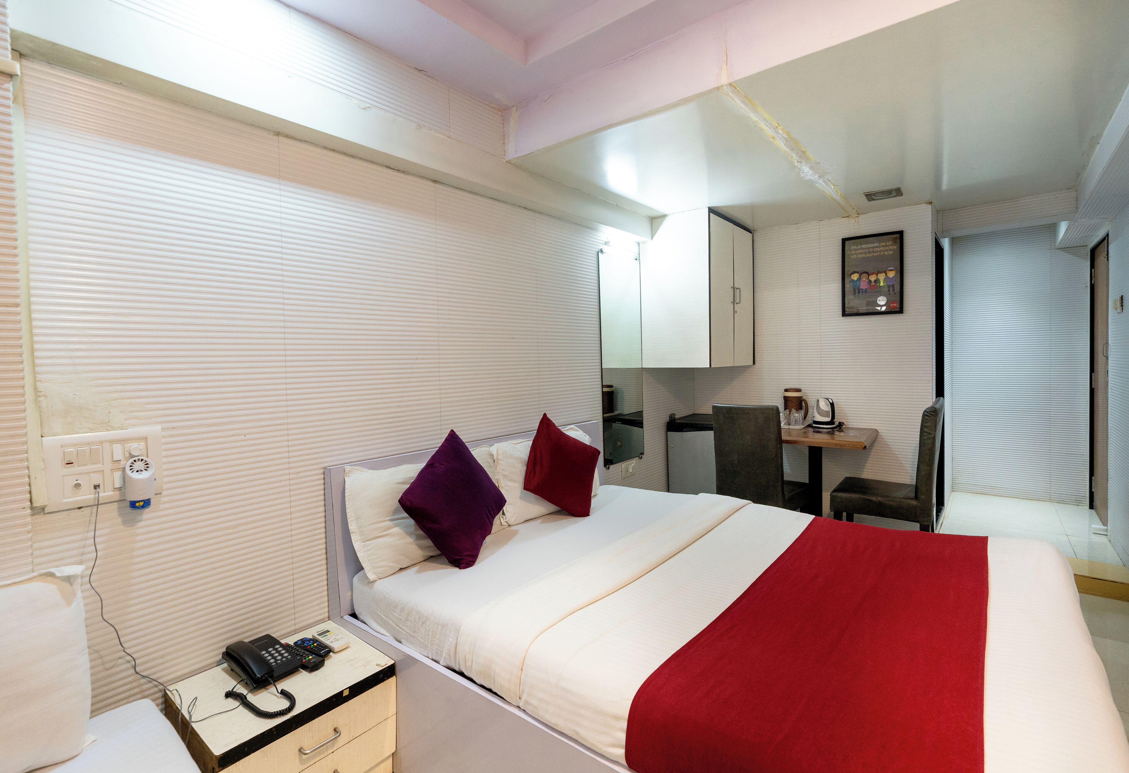 A hotel room with a bed, a desk, a chair, a telephone, and a coffee maker.