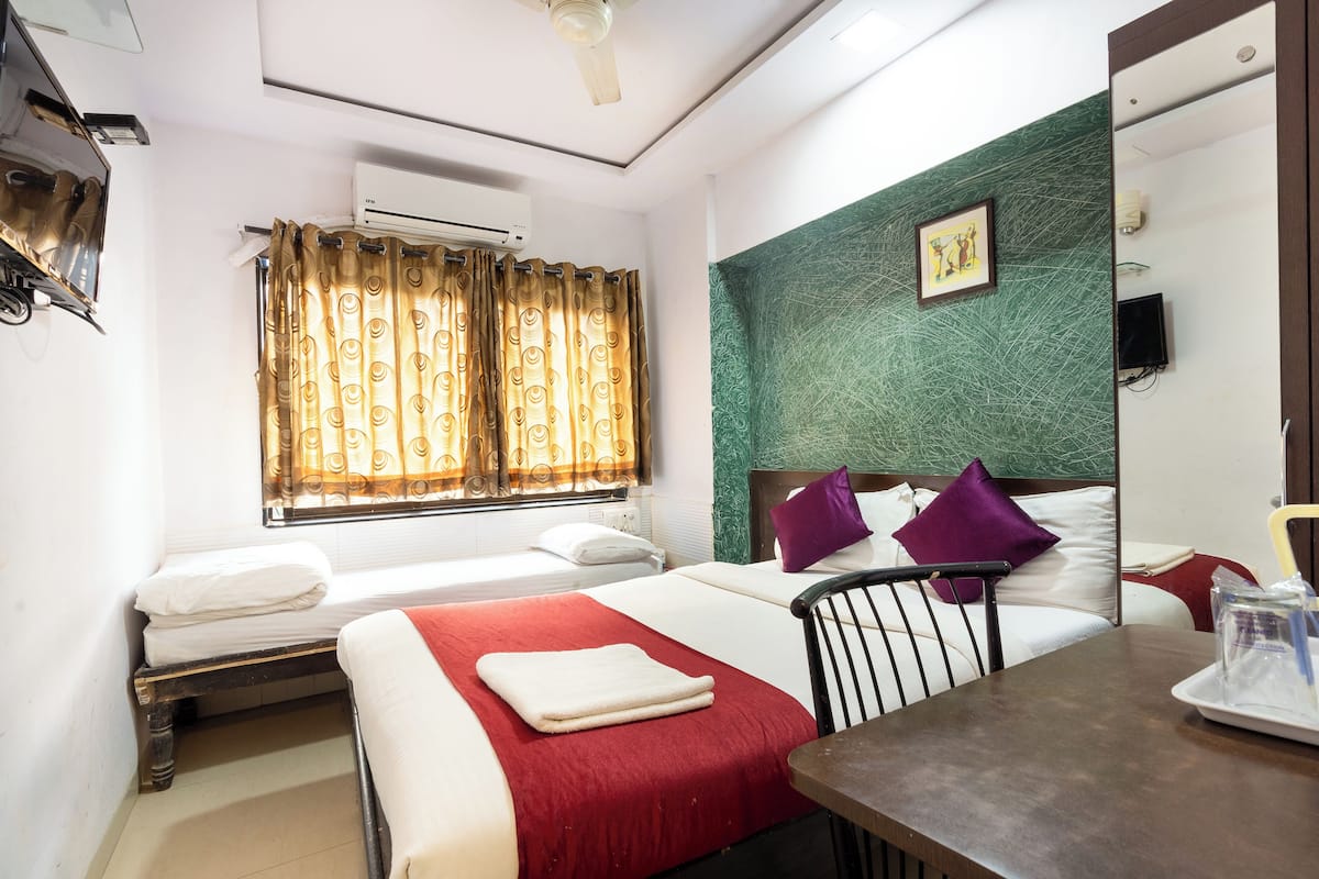 A hotel room with two beds, a dining table, a chair, an air conditioning unit, and a green textured wall.