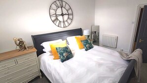 Ein Schlafzimmer mit einem Bett, einem Nachttisch, einer Wanduhr, einer Heizung und einer Tür.