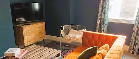 Una sala de estar moderna con un sofá, un televisor, un mueble de madera y un ventanal con cortinas.