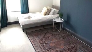 Ein Zimmer mit einem Bett, einem kleinen runden Tisch, einer Pendelleuchte und einem gemusterten Teppich.