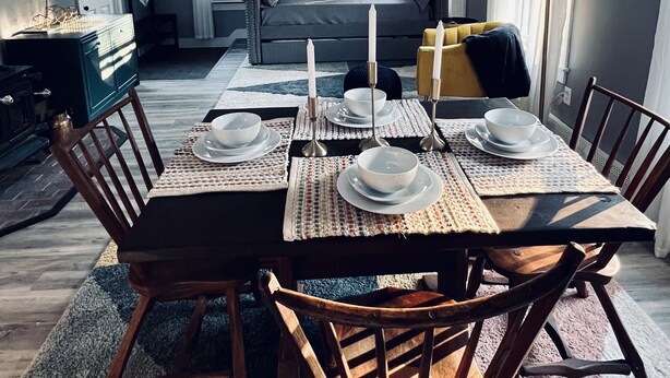 Een eethoek met een tafel voor vier personen, een plafondventilator en uitzicht op een woonkamer met een bank en een raam.