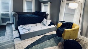 Een slaapkamer met een bed, een gele stoel, een zwart poef en een plafondventilator.