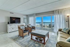 A spacious living room with a large flat-screen TV, wicker chairs, a beige sofa, and a view of the ocean through large sliding glass doors. - Direct beach access, oceanviews galore and has enough beds for your entire family! (Fernandina Beach)