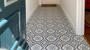 Un pasillo con baldosas de diseño, una puerta blanca con paneles de vidrio y cuadros en las paredes.