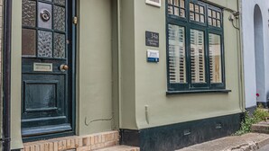Un edificio con fachada verde, una puerta negra con un panel de vidrio y un ventanal con contraventanas.