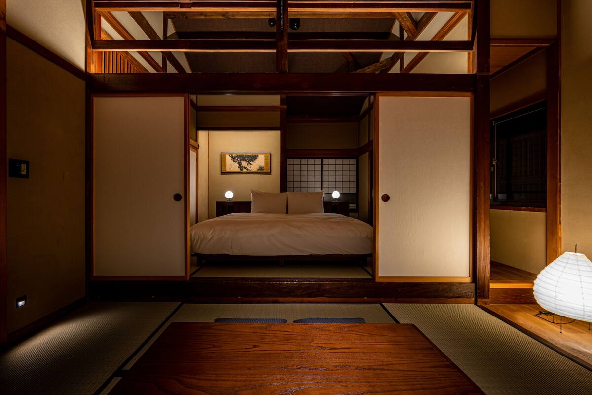 A traditional Japanese-style room with tatami flooring, a low wooden bed, and sliding doors.