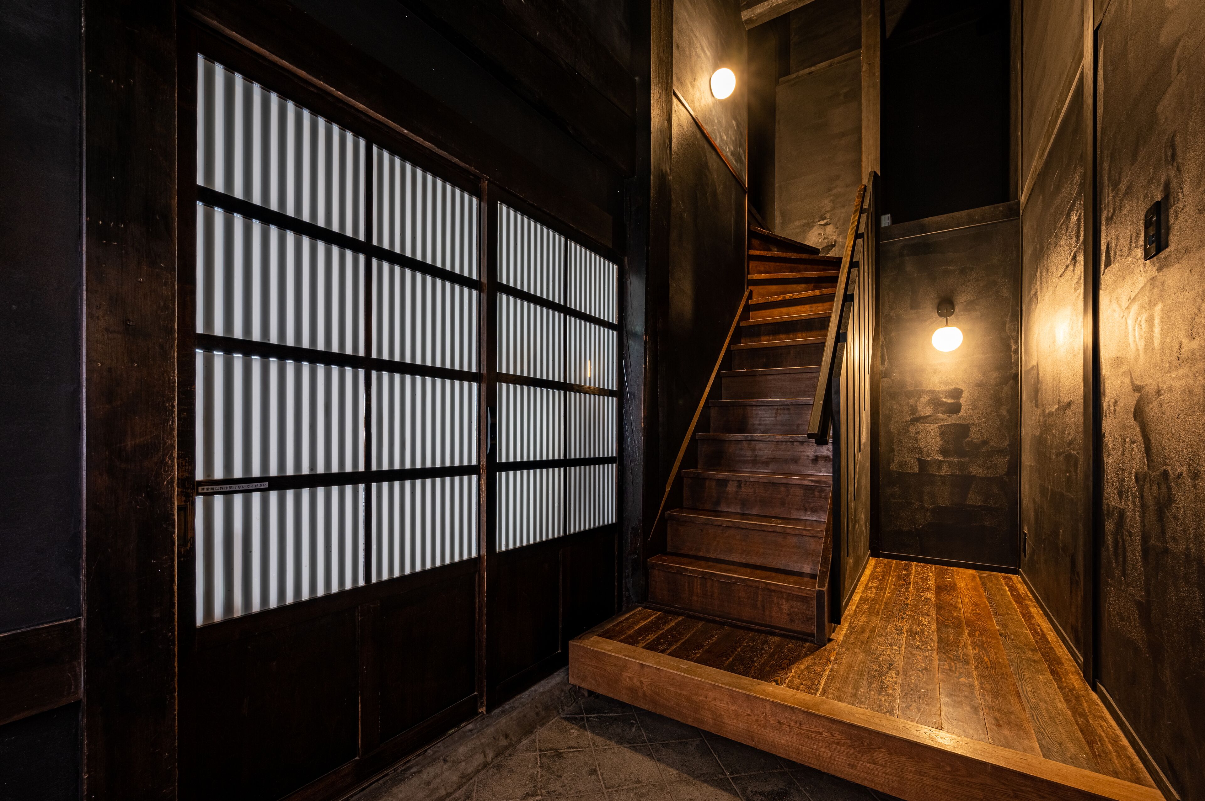 Una escalera de madera que lleva a una habitación oscura con una puerta corrediza tradicional.