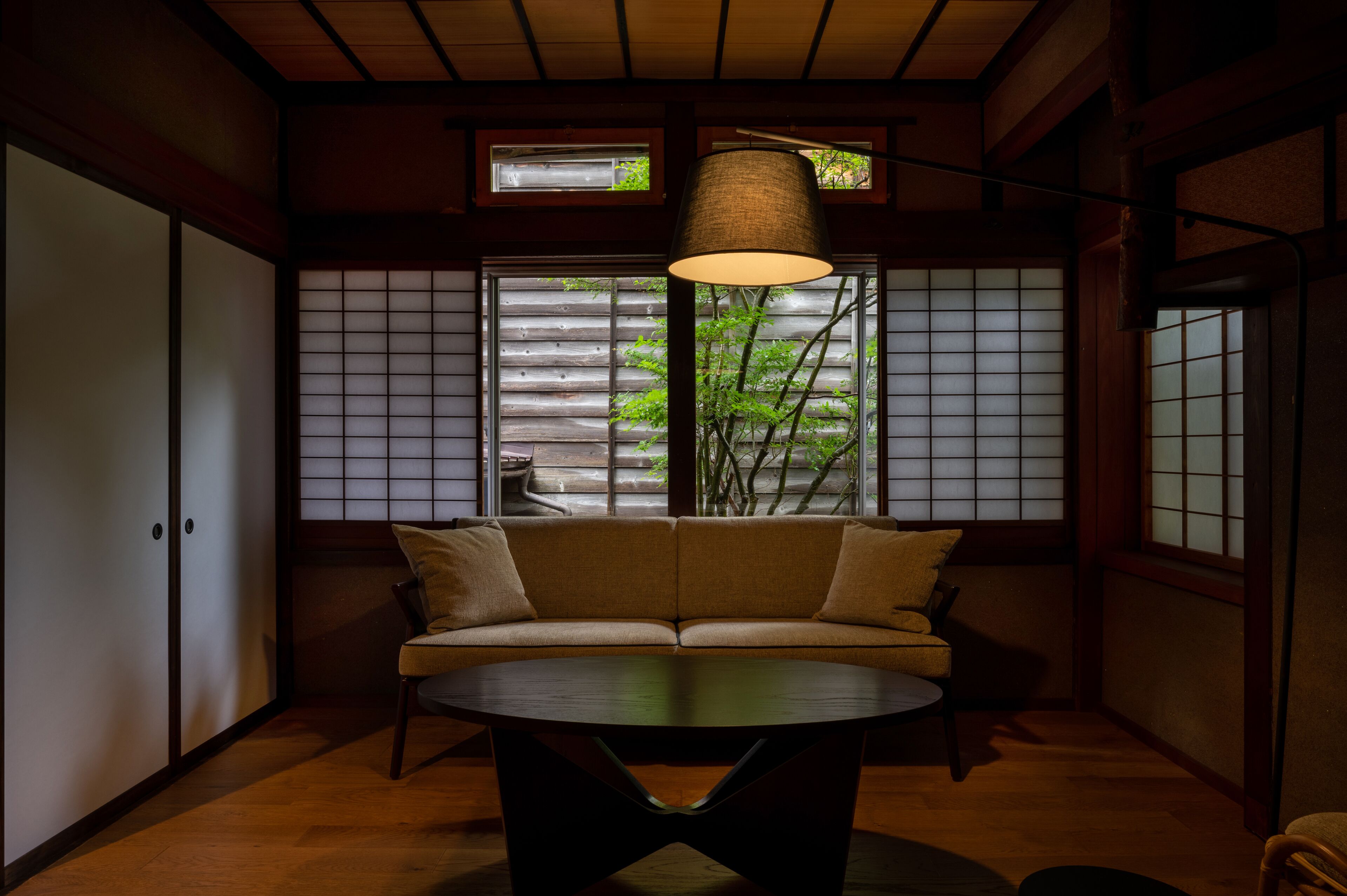 A traditional Japanese room with sliding doors, a sofa, a table, and a hanging lamp.