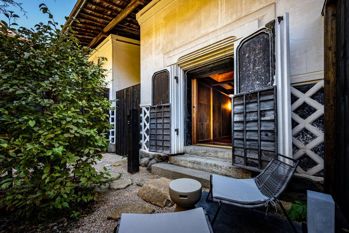 A building with a wooden exterior, a porch with two chairs, and a small table.