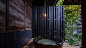A wooden cabin with a large stone bathtub in the center, surrounded by a wooden deck and a wooden fence. - BYAKU Narai (Shiojiri)