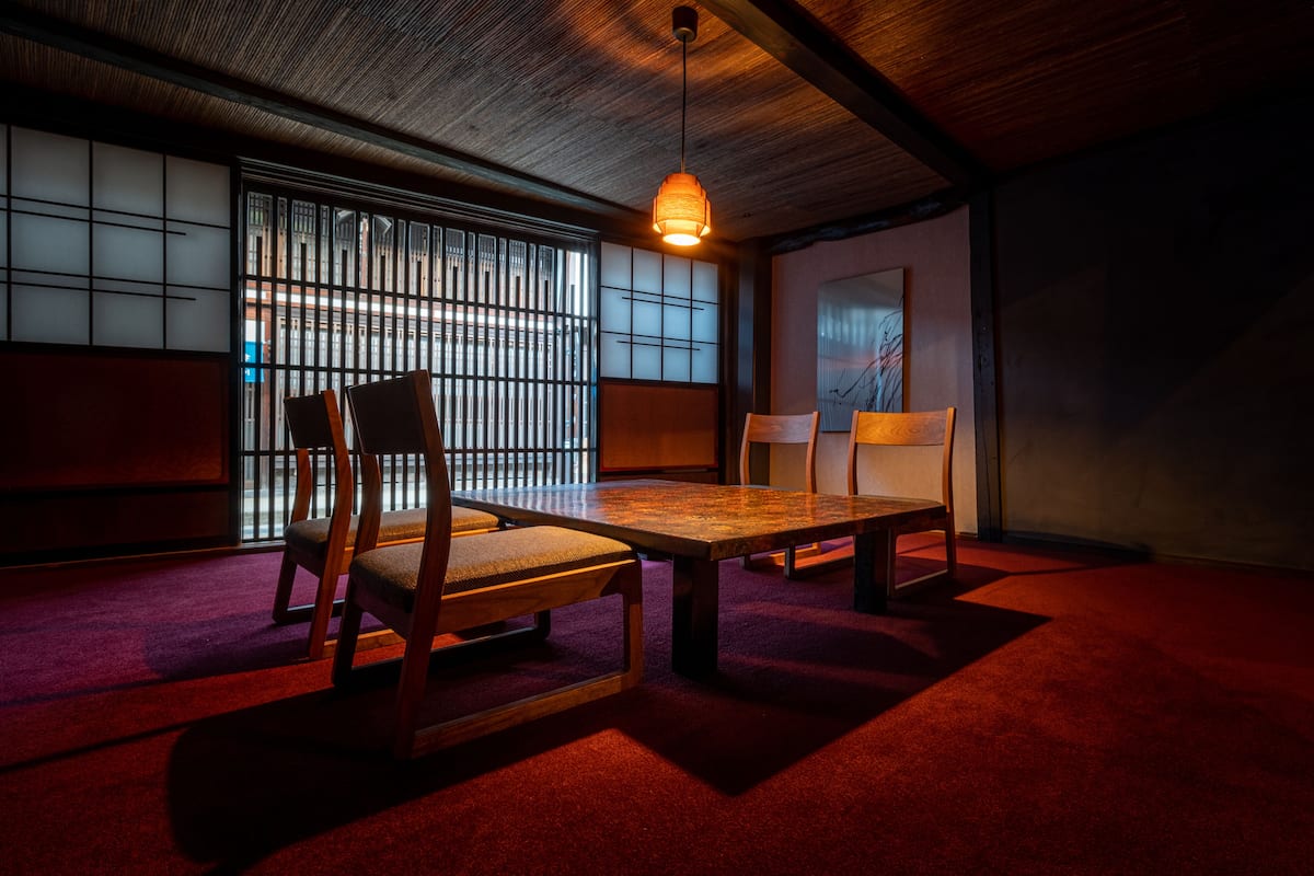 A traditional Japanese room with tatami flooring, a low wooden table, and a hanging light fixture.
