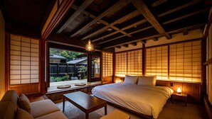 A traditional Japanese-style bedroom with tatami flooring, a low wooden bed, a futon sofa, and sliding shoji doors. - BYAKU Narai (Shiojiri)