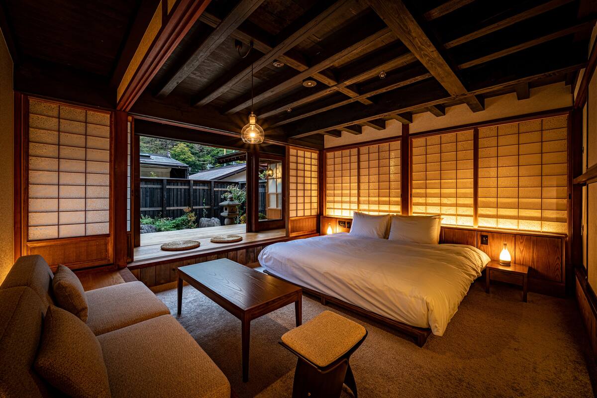 A traditional Japanese-style bedroom with tatami flooring, a low wooden bed, a futon sofa, and sliding shoji doors.