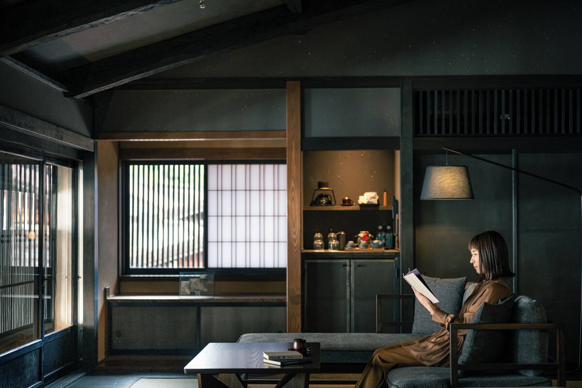 A room with a large window, a sofa, a table with books and a cup, and shelves with various items.