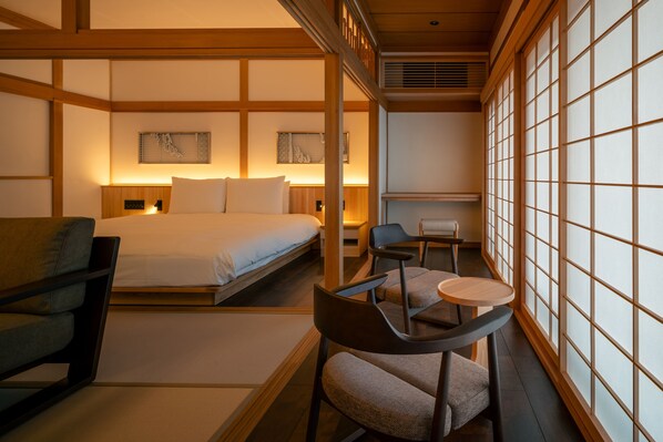 Una habitación de estilo japonés tradicional, con suelo de tatami, una cama baja, un escritorio con silla y puertas correderas.