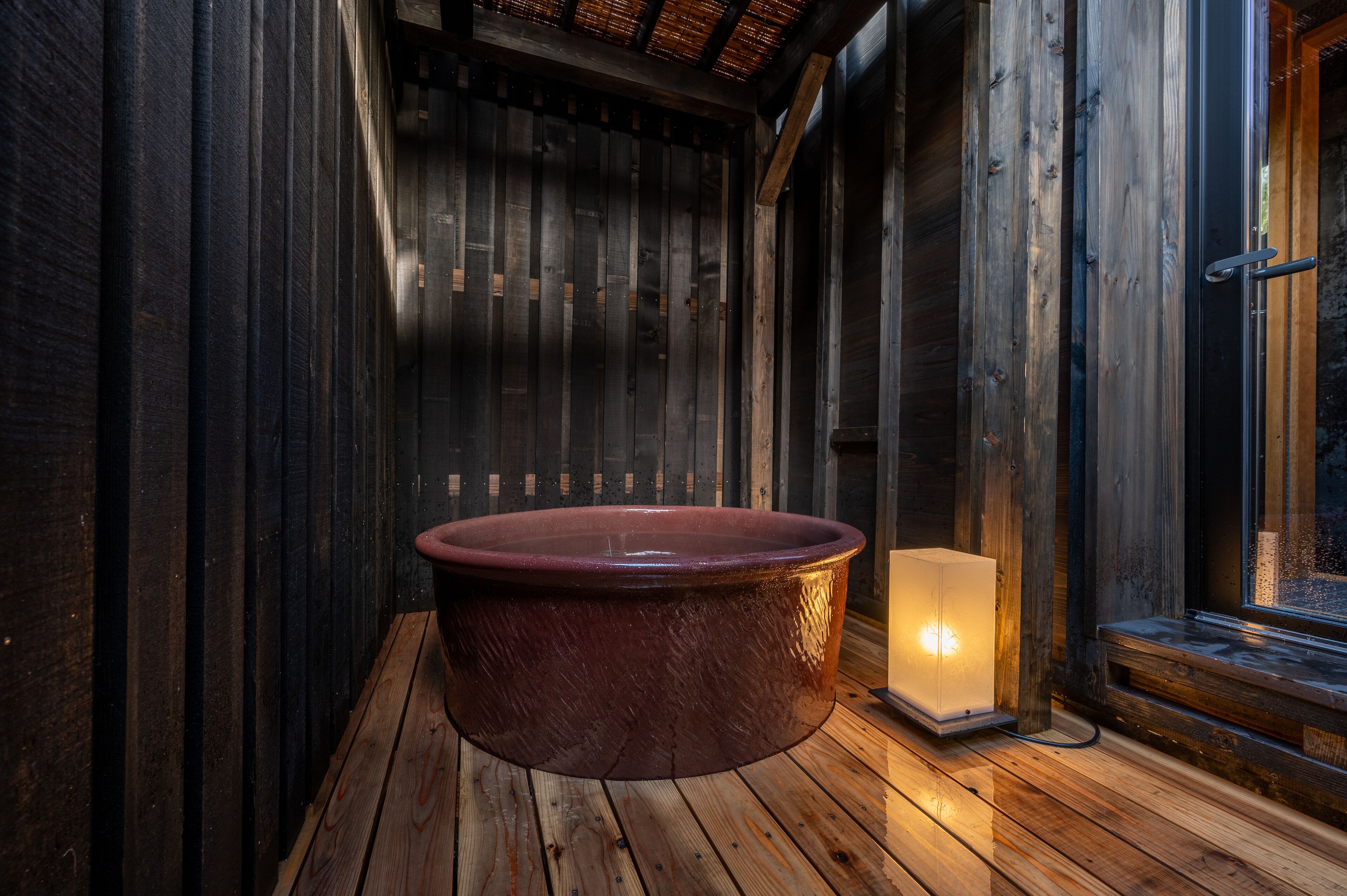 A wooden sauna with a large, round, dark-colored tub and a lit candle on the floor.