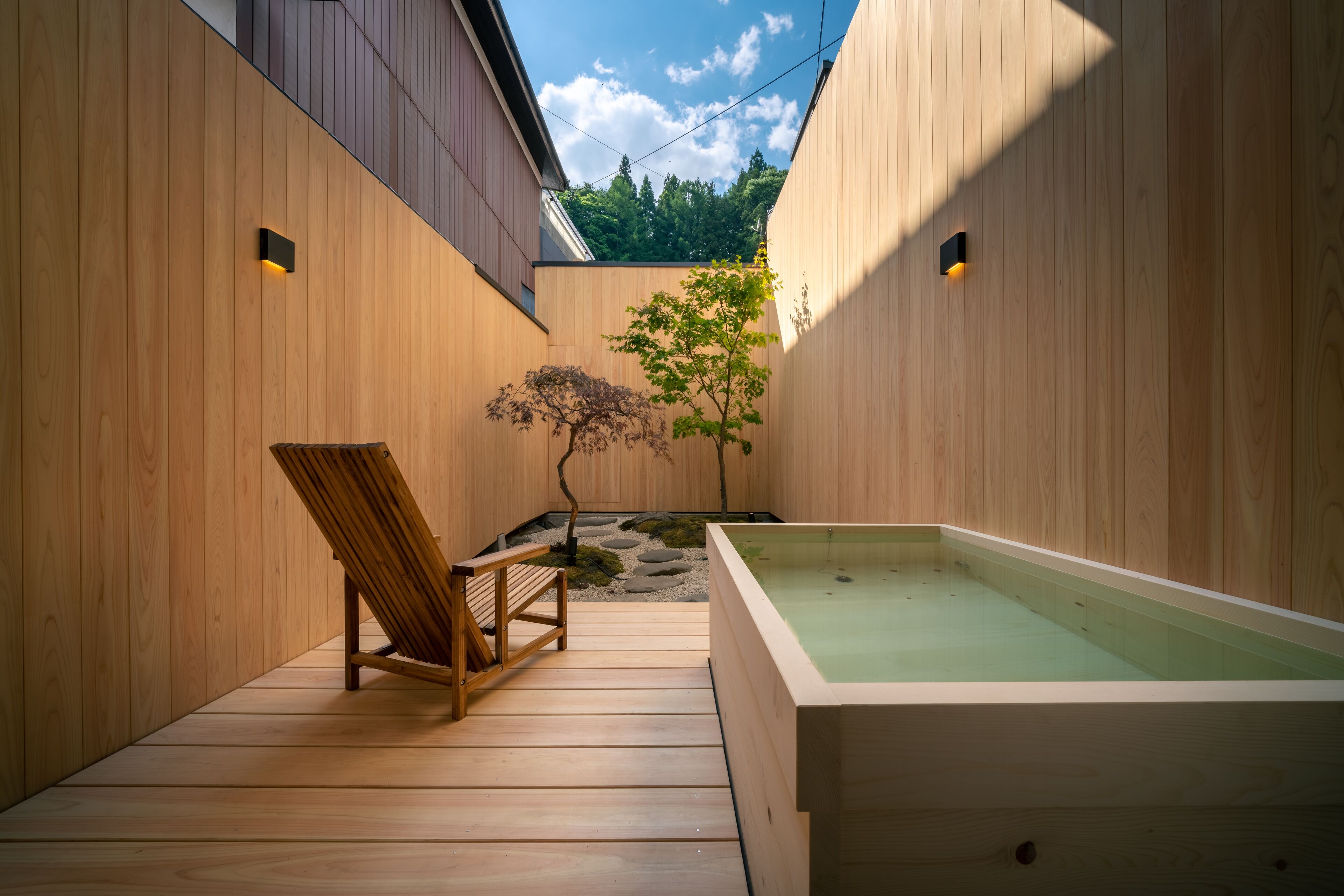 A wooden deck with a hot tub, a wooden chair, and a small tree.