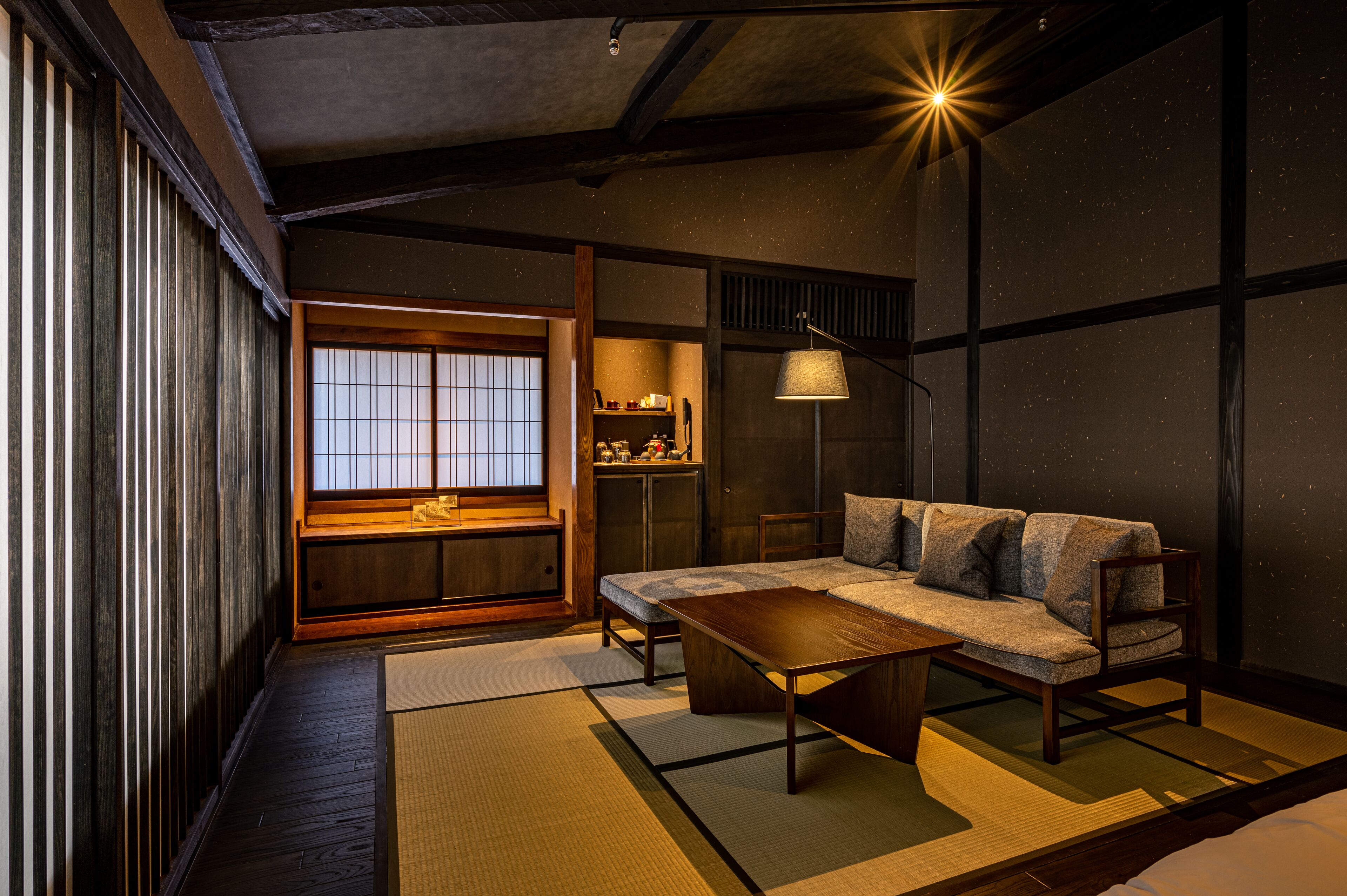 Una habitación japonesa tradicional con suelo de tatami, una mesa baja de madera, un sofá y una ventana con celosías shoji.